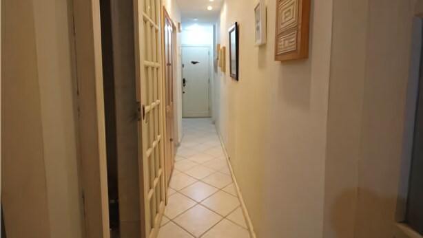 Un couloir avec un sol carrelé, une porte dotée d’un portail en métal et des tableaux encadrés accrochés au mur.