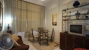 Un salon comprenant un canapé, un ventilateur, un téléviseur, une table à manger avec des chaises et une étagère décorative.