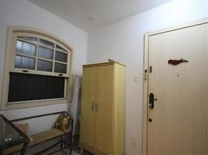 Um quarto com janela, um armário de madeira e uma porta.
