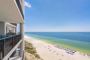 A beachfront hotel with a balcony overlooking the ocean, a sandy beach with umbrellas, and clear blue water. - The Oasis at Orange Beach, formerly known as Phoenix West II, Unit 1604 (Orange Beach)