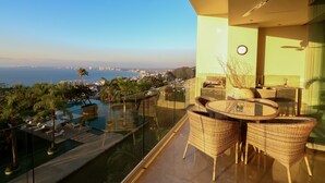 A balcony with a glass railing overlooking a swimming pool and cityscape.