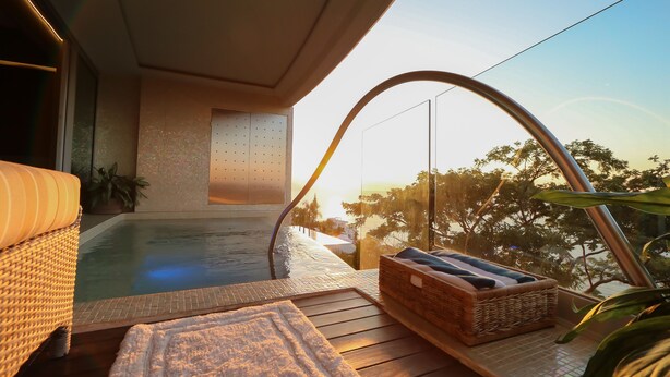 A balcony with a hot tub, wicker furniture, and a view of the sunset.