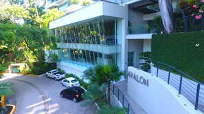 A modern building with a glass facade, surrounded by lush greenery and a well-maintained lawn. - Avalon 406, Modern luxurious smart condo with private pool & divine ocean views! (Puerto Vallarta)