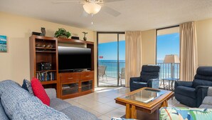 Sala de estar con televisor de pantalla plana, sofá, mesa de centro y balcón con vista al océano.