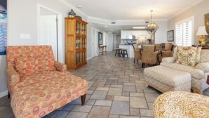 Un salón amplio con sofás estampados, un mueble de madera y una zona de cocina al fondo.