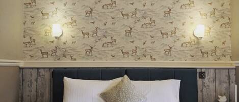 Un dormitorio con cama, cabecero, pared con estampado de animales y dos luces fijadas a la pared.