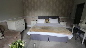 A bedroom with a large bed, a nightstand, a dresser, a chair, and a vase of flowers.