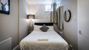 Un dormitorio ordenado con cama, lámpara de noche, espejo y un cuadro en la pared.