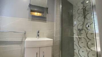 Un baño moderno con cabina de ducha de vidrio, un lavabo blanco y un espejo encima.