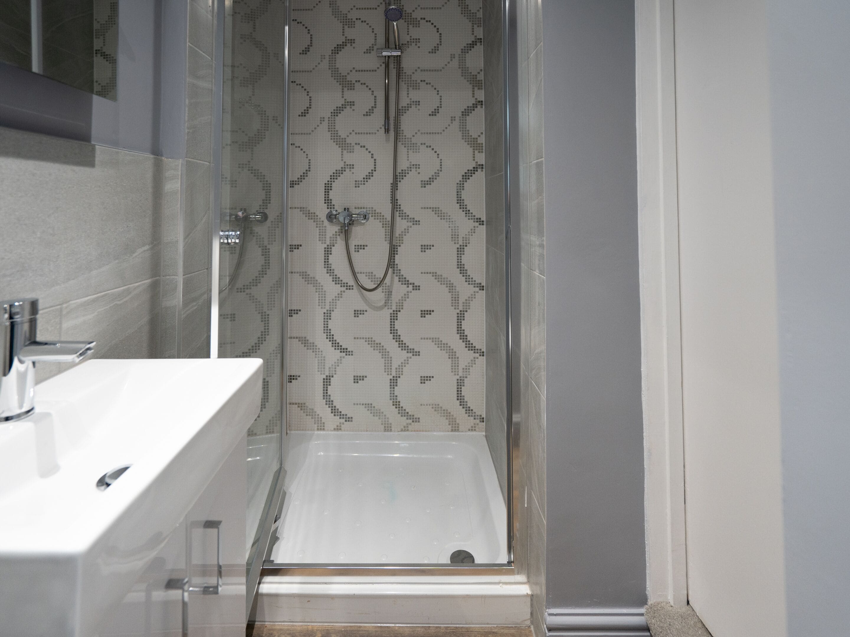 A modern bathroom with a glass-enclosed shower, a white sink, and a patterned tile backsplash.