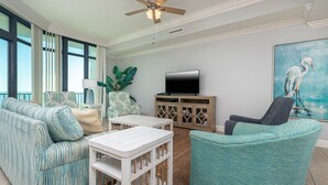 Una sala de estar con sofá, sillón, mesa de centro, televisión y un cuadro.