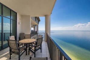 A balcony with a table and chairs, overlooking a calm sea and clear sky.