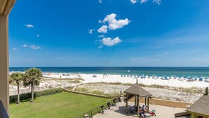 A beach view from a balcony with a gazebo, palm trees, and a sandy beach with umbrellas. - Second Floor Beach Front Balcony! 1BR 1BA @ Phoenix V (Orange Beach)