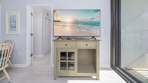 Een kamer met een grote flatscreen televisie op een kast, een houten stoel en een deur naar een andere ruimte.