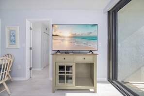 Een kamer met een grote flatscreen televisie op een kast, een houten stoel en een deur naar een andere ruimte.