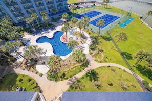 Un hotel con piscina, canchas de tenis y una zona ajardinada con palmeras.