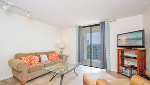 A living room with a sofa, a glass coffee table, a television, and a balcony with curtains.