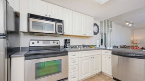 A kitchen with white cabinets, a stainless steel refrigerator, a microwave, a stove, a dishwasher, and a sink.
