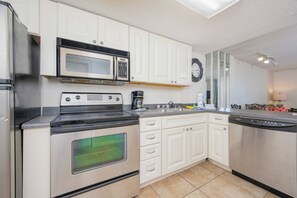 Una cocina con armarios blancos, un refrigerador de acero inoxidable, un microondas, una estufa, un lavavajillas y un lavaplatos.