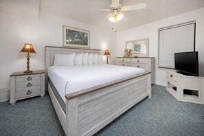 Ein Schlafzimmer mit einem Bett, zwei Nachttischen, einem Deckenventilator, einem Fernseher und einem Fenster mit Jalousien.