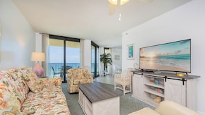 Un salon comprenant un canapé, des fauteuils, une table basse, un téléviseur et un balcon avec vue.