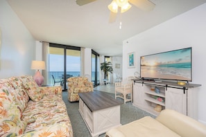 A living room with a sofa, chairs, a coffee table, a TV, and a balcony with a view. - *WEEKLY SPECIALS!* * Phoenix IV 1BR! 6th floor! (Orange Beach)