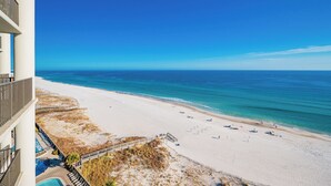 A beach view from a hotel balcony with a clear sky, sandy beach, and ocean. - The Oasis of Orange Beach 1003 (Orange Beach)