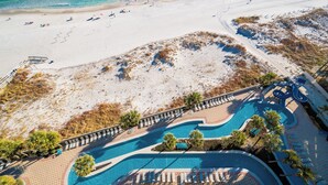 An aerial view of a beach resort with a swimming pool, beach chairs, and umbrellas. - The Oasis of Orange Beach 1003 (Orange Beach)