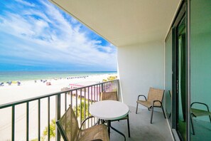 Ein Balkon mit Blick auf einen Strand, einem runden Tisch und zwei Korbstühlen.