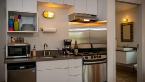 Uma cozinha moderna com eletrodomésticos de aço inoxidável, forno embutido e micro-ondas. Há uma pia, um escorredor de louça e uma prateleira com utensílios de cozinha.