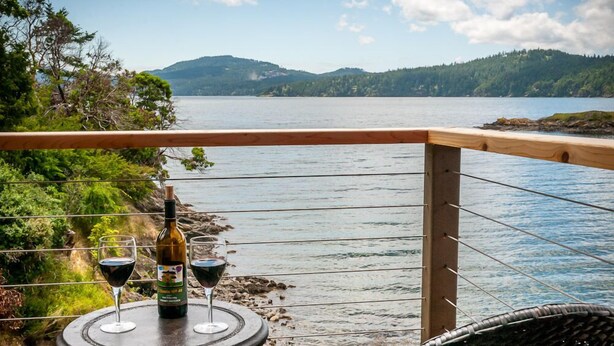 Uma mesa com uma garrafa e copos de vinho, com vista para um lago e montanhas ao fundo.