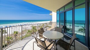 A balcony with a view of the beach, a round table, and chairs.