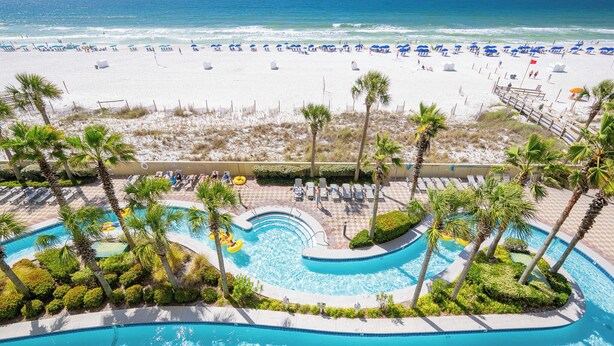 A pool area with palm trees, a beach, and a view of the ocean.