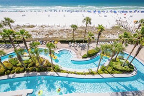 A pool area with palm trees, a beach, and a view of the ocean.