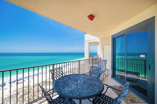 Un balcon avec une table et des chaises, donnant sur une plage et l’océan.