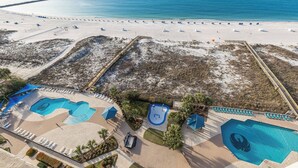 An aerial view of a beach resort with multiple swimming pools, sun loungers, and a sandy beach area.