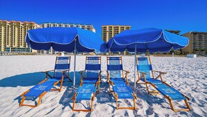 Beach chairs with blue canopies and a 'DO NOT SIT LEG REST' sign, set against a backdrop of high-rise buildings.