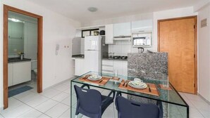 Cuina moderna amb armaris blancs, un microones integrat i una taula de dinar de vidre amb dues cadires.