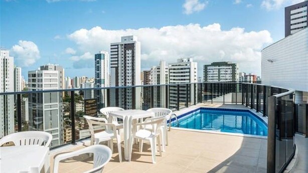 Una terrassa al terrat amb una piscina, cadires de plàstic blanc i un paisatge urbà al fons.