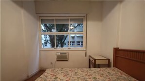 Un dormitorio con edredón estampado con motivos florales, una ventana con persianas, un calefactor y un cabecero de madera.