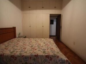 A bedroom with a bed, a nightstand, a wardrobe, and a door leading to another room.