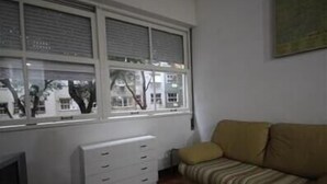 Una habitación con un sofá, un armario blanco y una ventana con persianas.