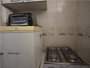 A compact kitchen with a white Electrolux refrigerator, a small toaster, and a gas stove. - GoHouse Leopoldo 602 (Rio de Janeiro)