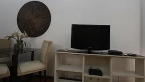 A living room with a TV on a stand, a dining table with chairs, and a decorative wall piece. - GoHouse Leopoldo 602 (Rio de Janeiro)