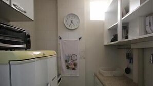 A compact kitchen with a white refrigerator, a clock on the wall, and a small window providing natural light. - GoHouse Leopoldo 602 (Rio de Janeiro)