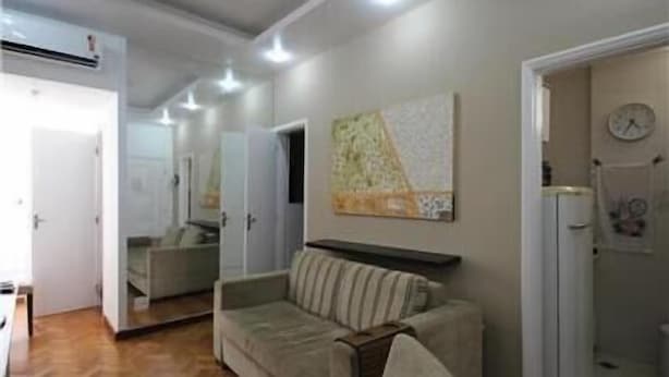 A living room with a sofa, a coffee table, and a refrigerator. There is a clock on the wall and a door leading to another room. - GoHouse Leopoldo 602 (Rio de Janeiro)