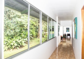A hallway with large windows, a tiled floor, and a view of greenery outside. - La Casa de la Montaña B&B (Monteverde)