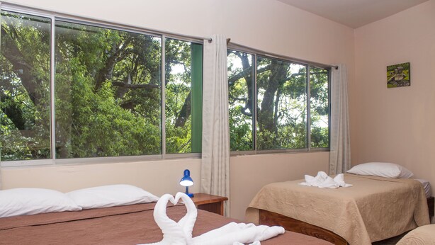 Een hotelkamer met twee bedden, een groot raam met uitzicht op bomen en een schilderij aan de muur.