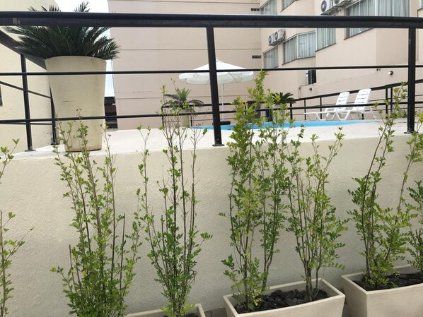 Un balcón con plantas en macetas, piscina y sillas de descanso.