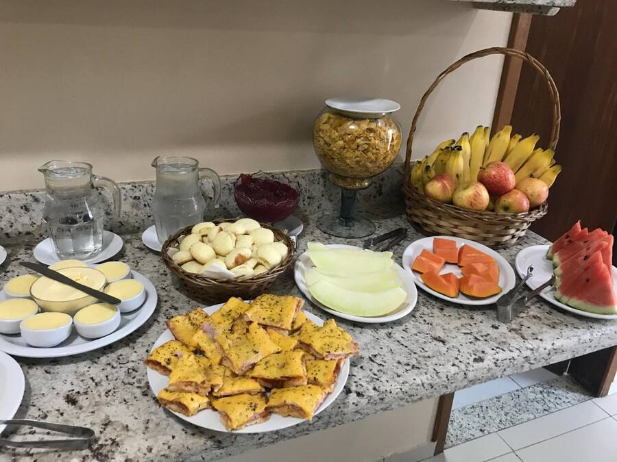 Um buffet de café da manhã com diversas opções de alimentos, incluindo pães, queijos, frutas e um jarro de água.